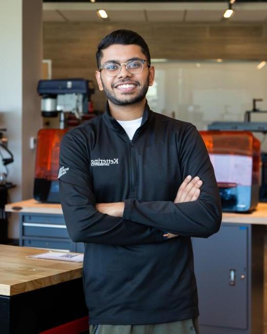 Kettering computer science alum Hemanth Tadapelli wears a Kettering jacket and stands in Kettering's Makerspace